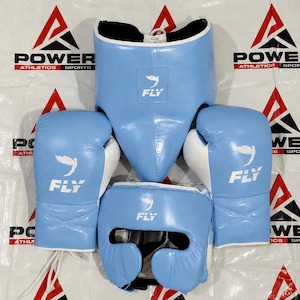 May include: A set of light blue and white boxing equipment including a pair of boxing gloves, a headgear, and a body protector. Each piece features the Fly logo, which depicts a stylized bird, and is constructed with smooth, durable material.