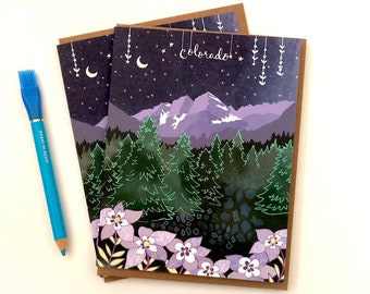 May include: Two rectangular greeting cards featuring a dark purple night sky with stars, a crescent moon, and the word "colorado" in white script. Below are purple mountains, green pine trees, and light purple columbine flowers. A blue pencil lies beside.