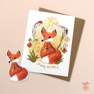 May include: A greeting card and sticker featuring a watercolor illustration of a fox with orange and white fur, adorned with decorative patterns. The card reads "Happy Birthday" in green script, and is accompanied by a brown envelope.
