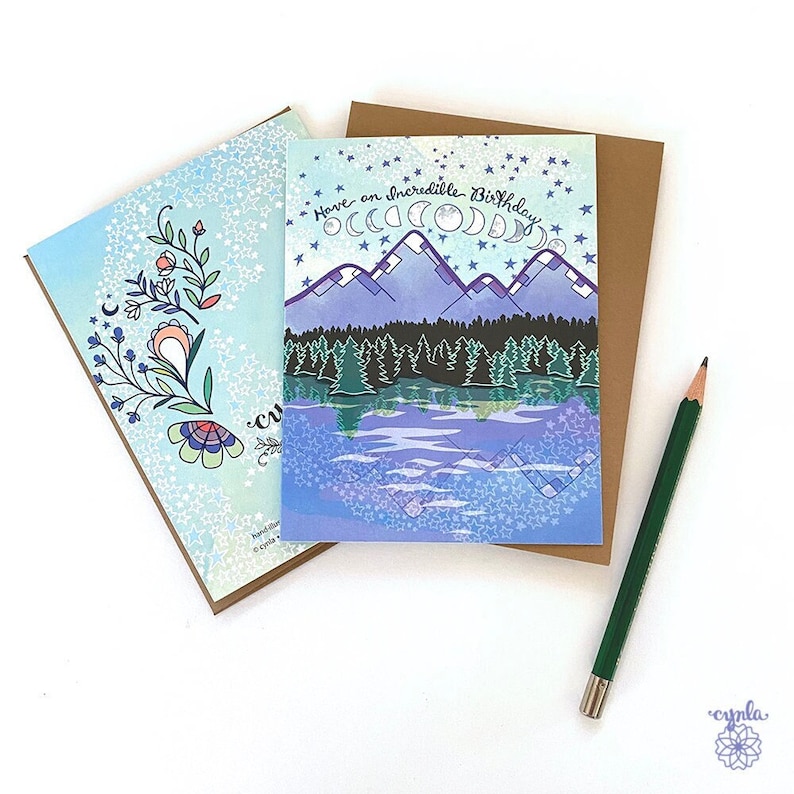 Mountain Shore Birthday Greeting Card May include: A blue and purple birthday card with a mountain scene and the text "Have an incredible birthday". The card is decorated with stars and moons.