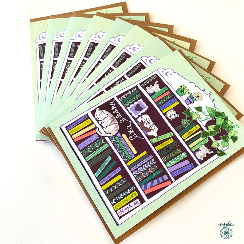 May include: A stack of greeting cards with a whimsical bookshelf design. Each card features a detailed illustration of a bookshelf with books, a sleeping cat, and the words "Happy Day". The cards have a light green border and a brown backing.