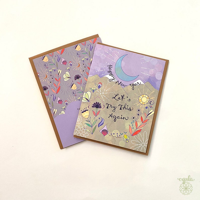 greeting cards with a mountain theme. The front of the card on top has a crescent moon and the words 'Happy New Year Let's Try This Again.' The front of the card on the bottom has a floral pattern with a purple background. funny new year greeting cards