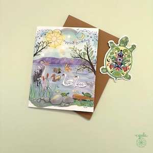 May include: A rectangular greeting card featuring a lake scene with a heron, ducks, and swans, with the text Happiest Birthday, paired with a brown envelope and a die-cut sticker of a green turtle decorated with colorful floral patterns.