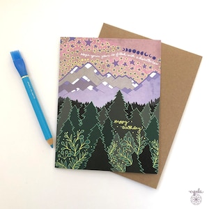 May include: A greeting card with a purple and pink mountain scene with stars and a forest in the foreground. The text on the card reads "Hope your year is filled with adventures. Happy Birthday."