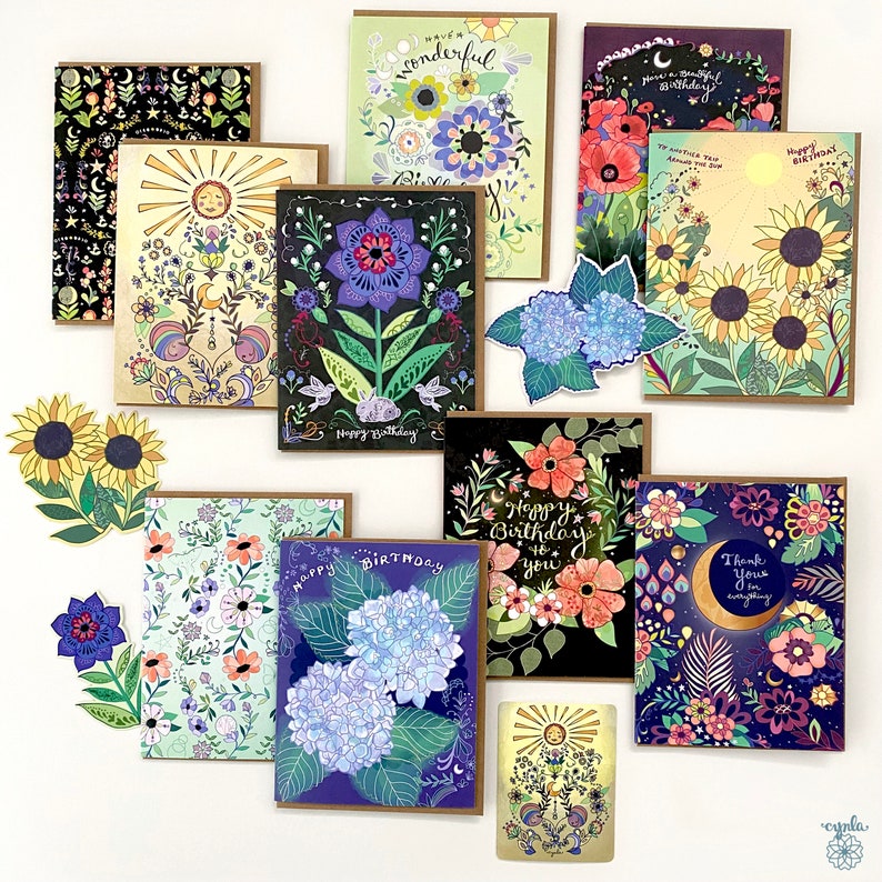 May include: A collection of decorative greeting cards with floral and celestial designs. The cards feature illustrations of sunflowers, hydrangeas, and other flowers, with text such as "Happy Birthday" and "Thank you". The cards have brown borders.