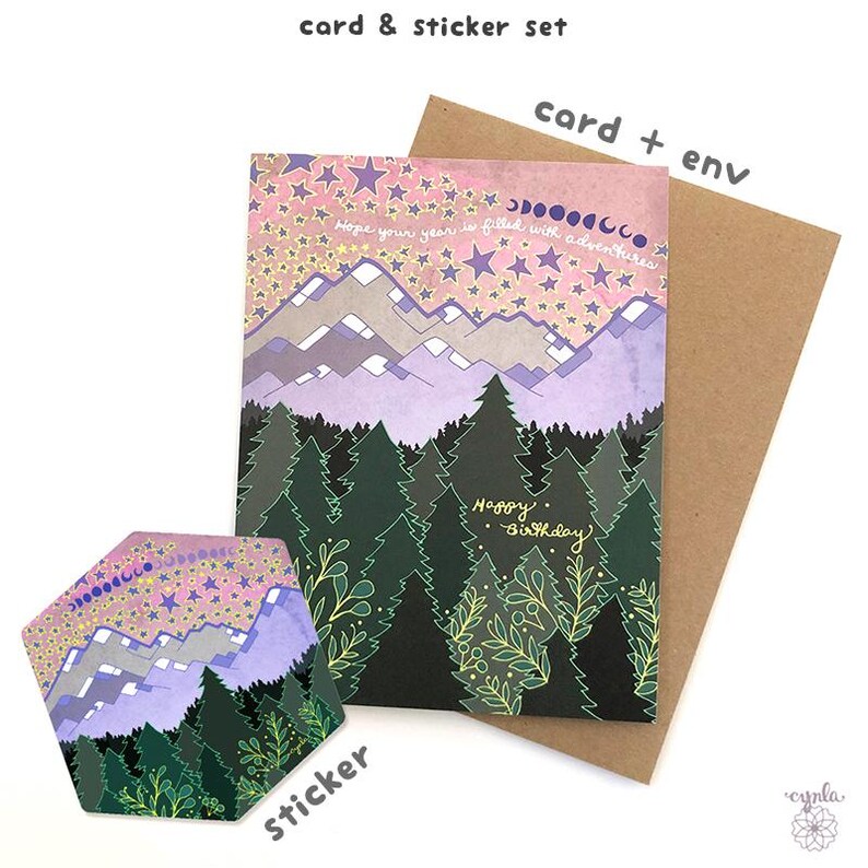 May include: A card and sticker set featuring a mountain and forest design. The card has a pink and purple sky with stars and the text "Hope your year is filled with adventures" and "Happy Birthday". The sticker has a similar design.
