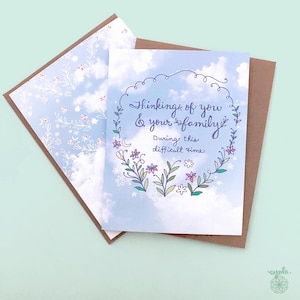 Puede incluir: Tarjeta de condolencia con fondo de cielo azul y una corona floral. La tarjeta dice: "Pensando en ti y en tu familia durante este momento difícil". El sobre tiene un estampado floral.