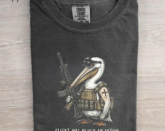 May include: A charcoal gray crew neck t-shirt featuring a graphic of a white pelican wearing tactical gear and night vision goggles while holding a rifle. The pelican has a cross tattoo on its wing. The text FLIGHT WAS NEVER AN OPTION is printed below.