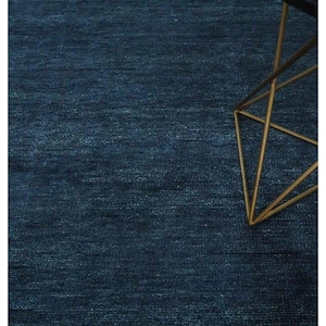 May include: A textured, navy blue rug fills most of the frame. A small, black-topped table with a gold geometric base is in the upper right corner. The rug's surface has subtle variations in color and texture.