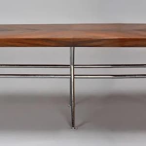 Peut inclure: Une table rectangulaire en bois avec une surface marron foncé et un motif en chevrons. La table est soutenue par un cadre en métal chromé avec quatre pieds. La table mesure environ 183 cm de long et 91 cm de large.