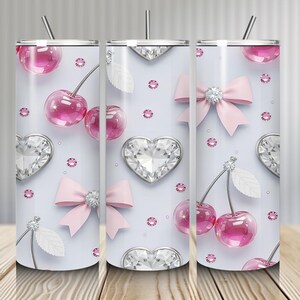 May include: A set of three stainless steel tumblers with a light blue background. The tumblers are decorated with pink cherries, diamond hearts, pink bows, and pink rhinestones. Each tumbler has a silver lid and a silver straw.