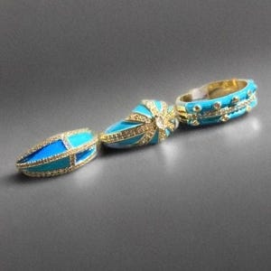 Young woman wearing turquoise enamel statement rings with gold tone details, stacked ring set styled for everyday fashion, close-up lifestyle hand photo on neutral background.
