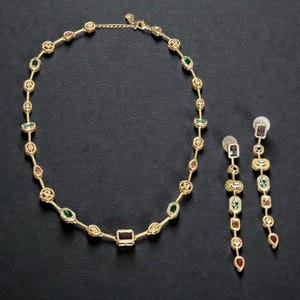 May include: A gold-tone necklace and matching drop earrings set. The necklace features a delicate chain interspersed with various small, multi-colored gemstones in teardrop, oval, and rectangular shapes. The earrings mirror this design.