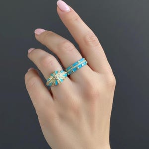Close-up of turquoise enamel ring set on a woman’s hand, stylish gold tone statement jewelry.