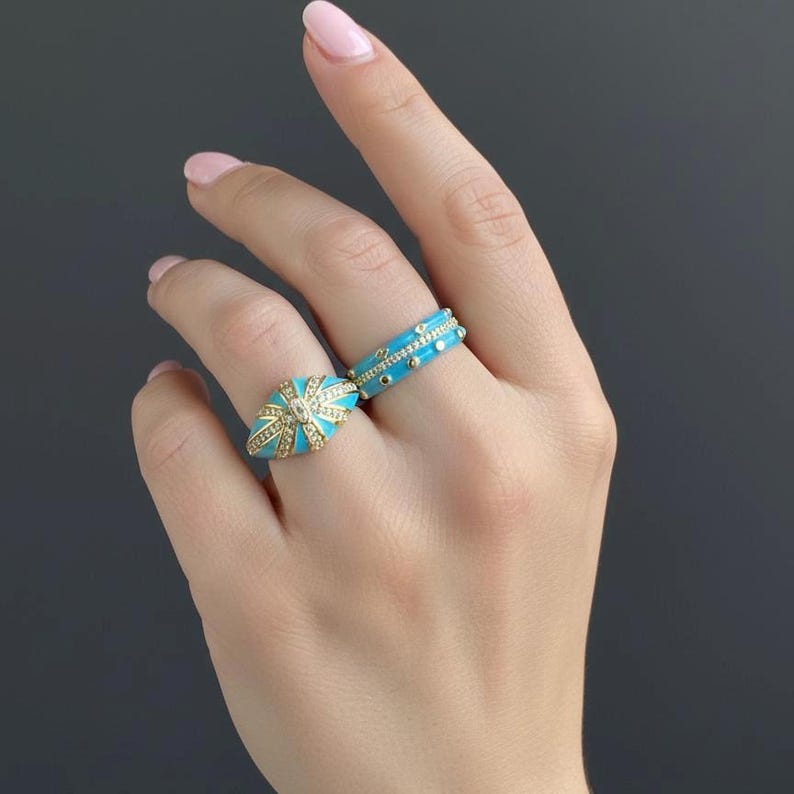 Close-up of turquoise enamel ring set on a woman’s hand, stylish gold tone statement jewelry.