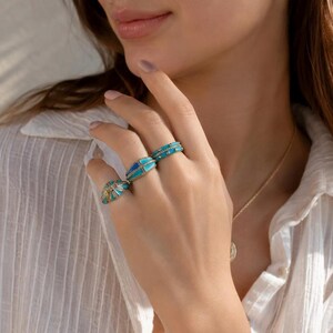 Young woman wearing turquoise enamel statement rings with gold tone details, elegant everyday jewelry lifestyle photo.