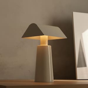 May include: A modern, beige table lamp with a geometric design. The lamp features a rectangular base that tapers upwards, a cylindrical neck, and a flat, angled shade. The lamp is approximately 12 inches tall.