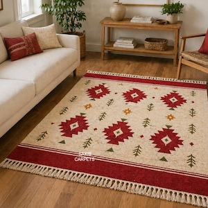May include: A rectangular area rug with a cream-colored background and a repeating pattern of red geometric shapes, green trees, and yellow stars. The rug has a red border with white stripes and fringe.