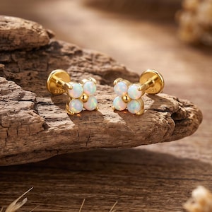 May include: A pair of gold-tone stud earrings, each featuring four small, round, iridescent white opals arranged in a flower-like cluster. The metal settings are stamped with 925, indicating sterling silver construction with a gold finish.
