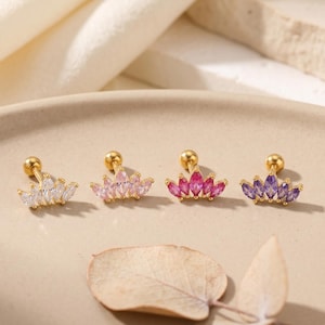 May include: Four gold-tone stud earrings, each featuring a crown-like design with five marquise-cut stones. The stones are arranged in a fan shape, with colours ranging from clear white to light pink, dark pink, and purple, all set on gold posts.