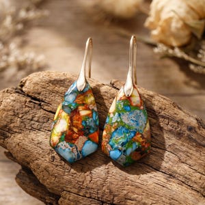May include: A pair of drop earrings featuring teardrop-shaped stones with a vibrant, multicolored mosaic pattern of blue, green, orange, and white. The stones are suspended from simple gold-toned metal hooks, creating a distinct, polished look.
