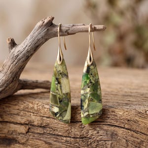 May include: A pair of drop earrings featuring elongated, triangular-shaped pendants made of a mosaic of green and olive-colored stone fragments. The pendants are suspended from simple gold-toned metal hooks that attach to the top of each piece.