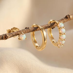 May include: A set of three gold-toned earrings featuring one stud earring with a single round opal, one plain gold hoop earring, and one gold hoop earring adorned with five round opal stones, all marked with S925 on the stud backing.