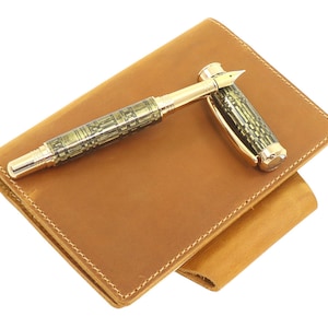 May include: A brown leather notebook with a gold and green patterned fountain pen on top.