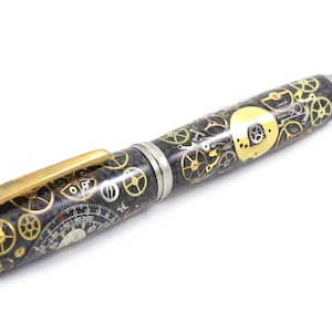 May include: A pen with a steampunk design. The pen features a black barrel with gold and silver gears, a gold clip, and a silver tip. The pen has a unique, detailed design.