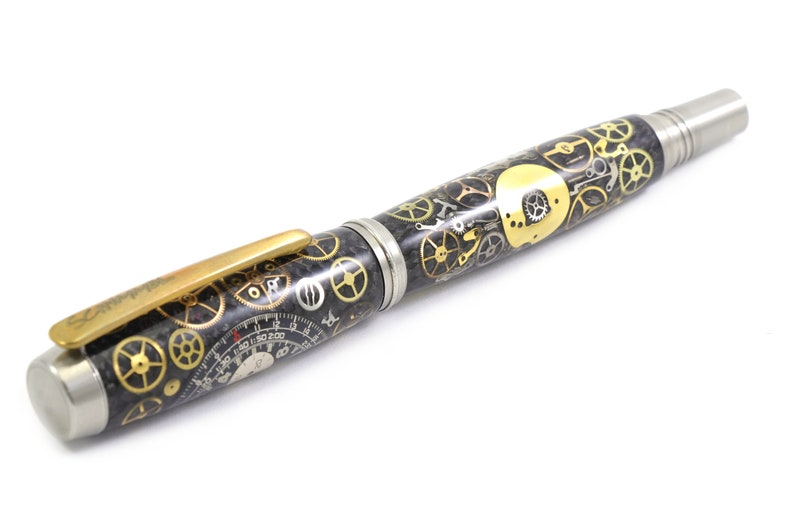 May include: A pen with a steampunk design. The pen features a black barrel with gold and silver gears, a gold clip, and a silver tip. The pen has a unique, detailed design.