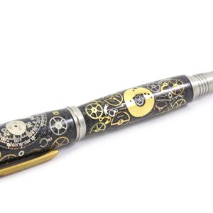 May include: A detailed pen with a steampunk design. The pen features a black and silver body with gold-colored gears and clock faces. The pen has a silver tip and a gold-colored clip.