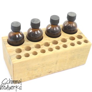 May include: Wooden organiser with multiple holes for storing small bottles. Four amber glass bottles with black caps are in the organiser. The organiser is made of light wood with a natural finish.