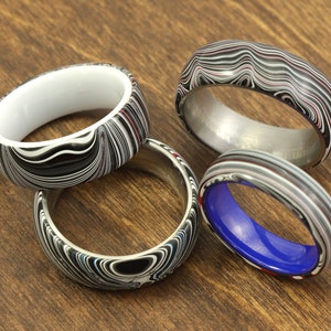 May include: Four rings with a black, white and red marbled pattern. One ring has a white interior, one has a blue interior, and one has a silver interior. The fourth ring has a silver band.