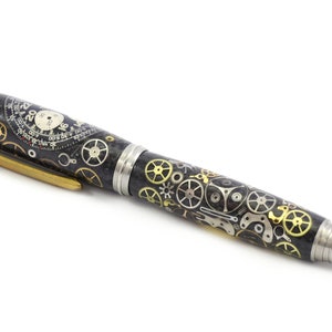 May include: A black pen with a detailed design of watch gears in silver and gold. The pen has a silver tip and a gold clip. The pen's body is covered in a pattern of watch parts.