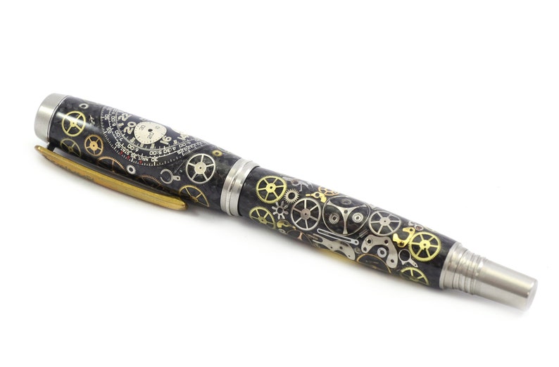 May include: A black pen with a detailed design of watch gears in silver and gold. The pen has a silver tip and a gold clip. The pen's body is covered in a pattern of watch parts.