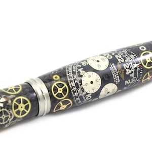 May include: A pen with a black and silver body, adorned with watch gears and clock faces. The pen features a Breitling Chronometre Automatic design with white clock faces and gold gears.