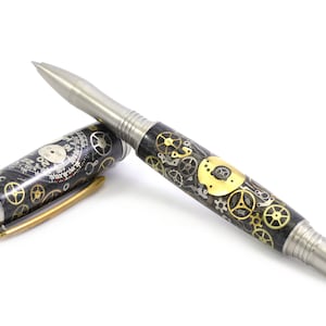 May include: A fountain pen with a stainless steel nib and accents. The pen's barrel is decorated with a pattern of gears in gold and silver tones, and the cap features a clock face design. The pen is lying on a white surface.
