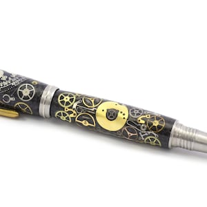 May include: A detailed pen with a steampunk design. The pen features a black barrel adorned with gold and silver gears, a silver tip, and a gold clip. The pen's design incorporates elements of watchmaking.