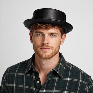 Puede incluir: Un sombrero de cuero negro con la parte superior y el ala planas. El sombrero lo lleva una persona que lleva una camisa a cuadros verde y negra. El diseño del sombrero es de estilo clásico, adecuado para diversas ocasiones.
