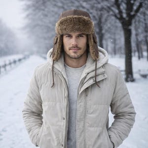 May include: A person wearing a brown fur-lined winter hat with ear flaps and a light beige quilted jacket. The hat is made of brown leather and faux fur. The jacket has a hood and a zipper closure. The background is a snowy winter scene.