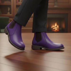 May include: A pair of vibrant purple Chelsea boots featuring smooth uppers, rounded toes, and dark brown elastic side panels. The boots have a low, flat heel and a dark brown sole, worn with dark grey trousers that fall just above the ankle line.