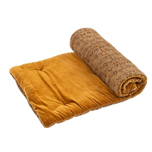 Könnte beinhalten: Eine aufgerollte Decke mit einem braunen und goldenen Blumenmuster liegt neben einer flachen, senfgelben Samtdecke. Die aufgerollte Decke liegt neben einer flachen, senfgelben Samtdecke. Die flache Decke hat eine einfarbige senfgelbe Farbe.