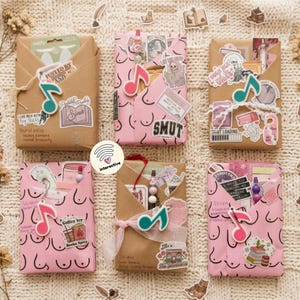Op de afbeelding: Zes rechthoekige pakketjes verpakt in bruin of roze papier, versierd met diverse stickers, muzikale noot-bedeltjes en handgeschreven tekst. De pakketjes zijn gerangschikt in twee rijen van drie en bevatten verschillende grafische ontwerpen.