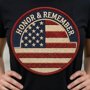 Może przedstawiać: Okrągła naszywka z flagą amerykańską i napisem "HONOR & REMEMBER" w okrągłym wzorze. Naszywka ma niebieską obwódkę z białym tekstem, niebieskie pole gwiazd i czerwono-białe paski. Naszywka jest na czarnej koszulce.