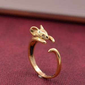 May include: A gold-colored ring featuring a mouse design. The ring wraps around the finger with the mouse's head and paws on one side and the tail on the other. The mouse has detailed ears and a textured face.