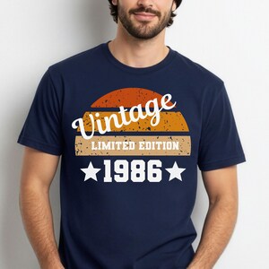Op de afbeelding: Marineblauw T-shirt met een vintage design. Het ontwerp toont het woord "Vintage" in een scriptlettertype, boven een retro zonsondergangafbeelding, de tekst "LIMITED EDITION" en het jaar "1986" met sterren. Een klassiek T-shirt.
