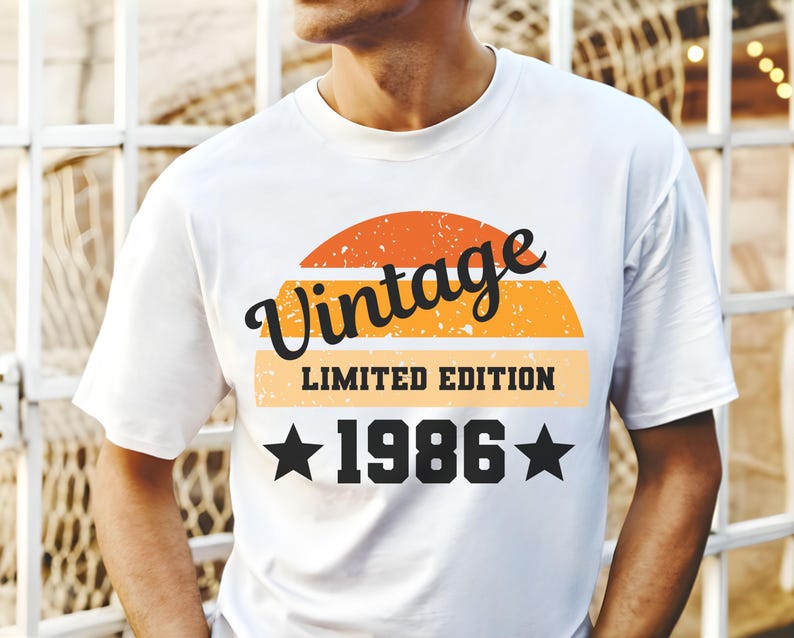 Op de afbeelding: Wit t-shirt met een retro design. Het ontwerp bevat het woord "Vintage" in zwart script boven een zonsondergangafbeelding. Daaronder staan de woorden "LIMITED EDITION" en het jaar "1986" met steraccenten.
