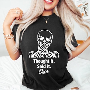 Puede incluir: Camiseta negra con un gráfico de esqueleto blanco cubriendo su boca. El texto "Thought it. Said it. Oops." está impreso debajo. Una prenda casual para el día a día.