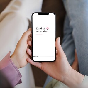 May include: A smartphone displays the text "Kind of geen kind" in black, with a pink flower graphic. The phone is held by a person, with a pink sleeve visible. The background shows light-colored pants and blue jeans.
