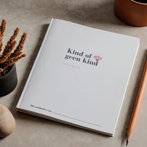 May include: A white workbook with the text "Kind of geen kind" and a floral design. A pencil, a small potted plant, and a decorative stone are next to the book. The workbook is on a neutral surface.
